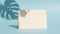 Blank greeting card casting a shadow from a monstera leaf on a pastel blue background Royalty Free Stock Photo