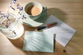 Blank greeting card and envelope of natural paper, pen, coffee cup and a glass vase with gentle sunlight reflections on a wooden Royalty Free Stock Photo