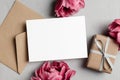 Blank greeting card mockup with envelope, flowers and gift box on grey, top view, copy space