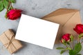 Blank greeting card with red rose flowers and gift box on gray background. Wedding invitation. Mock up. Flat lay. Womans Royalty Free Stock Photo