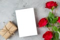 Blank greeting card with red rose flowers and gift box on gray background. Wedding invitation. Mock up. Flat lay. Womans Royalty Free Stock Photo