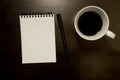 Blank gridded spiral notepad with pen and cup of coffee - on dark timber