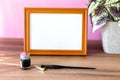 Blank landscape wooden frame beside a small houseplant and calligraphy tools, painting or artwork display mockup