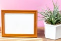 Blank landscape wooden frame beside a small houseplant, painting or artwork display mockup