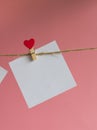 Blank message card attached with a wooden clothespin with a red heart on a rope on a pink background Royalty Free Stock Photo