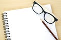 Blank note book, eye glasses and pencil on wood background