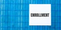 Blank note pad with ENROLLMENT text on blue wooden background Royalty Free Stock Photo