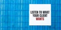 Blank note pad with LISTEN TO WHAT YOUR CLIENT WANTS text on blue wooden background