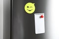 Blank note and sticker with funny face on refrigerator door. Royalty Free Stock Photo