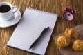 Blank notebook, alarm clock,eclairs and coffee cup.