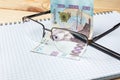 Blank notebook, glasses and ukrainian money on a wooden background. Banknote of 1000 hryvnia. Hryvnia UAH.. Close-up