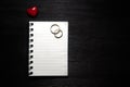 Blank notebook with heart and wedding rings on black background