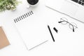 Blank notebook page is on top of white office desk table with laptop computer, cup of coffee and supplies. Top view with copy Royalty Free Stock Photo