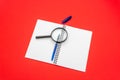 Blank notebook and pen on red background. Magnifying glass on top of notepad Royalty Free Stock Photo