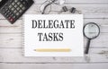 Blank notebook with text DELEGATE TASKS on the white background with calculator and office tools