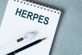 Blank notebook with thermometre and pen on table. HERPES word