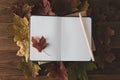 Blank notebook on a wooden work table with autumn leaves. Top view. Copy space