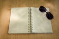 Blank notebooks with sunglasses are placed on wooden table. There is a shadow of sunlight reflected on the notebook.