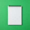 A blank notepad with a black spiral binding is centered on a vibrant green background. Royalty Free Stock Photo