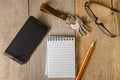 Blank notepad, key chain, eye glasses and mobile phone on wooden