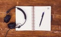 Blank notepad with a pen and headphones on wooden table background. Notepad, pen and headphones. Top view. insta look