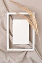 Blank paper card mock up in empty picture frame border, dried meadow grass on neutral beige fabric background. Aesthetic