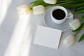 Blank paper card mockup, coffee cup, saucer, white tulip flowers bouquet on neutral marble table background with Royalty Free Stock Photo