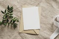 Blank paper card mockup, envelope, green branch, silk ribbon on linen tablecloth. Wedding invitation card design, greeting card