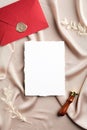 Blank paper card and red envelope with wax seal on silk fabric background. Flat lay, top view, copy space. Wedding invitation card Royalty Free Stock Photo