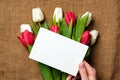 Blank paper card in womans hands on rustic burlap canvas with tulips flowers. Greeting card for International Womans Day, Mothers Royalty Free Stock Photo