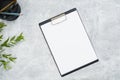 Blank paper clipboard mockup on concrete desk with stationery and branch with green leaves. Flat lay, top view, overhead. Business