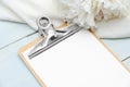 Blank paper clipboard mockup with white peony flowers on blue wooden table. Top view. Wedding planner, to do list, checklist Royalty Free Stock Photo