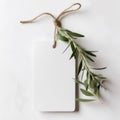 Blank paper gift tag, label mockup with rope and olive tree branch on white table. Created with Generative AI. Royalty Free Stock Photo