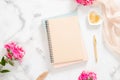 Blank paper notebook, pink flowers, pastel blanket and golden accessories on marble background. Flat lay, top view rose gold home