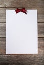 Blank paper sheet with burgundy bow on wooden background Royalty Free Stock Photo