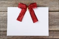 Blank paper sheet with red bow on wooden background