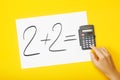 Blank paper with task 2 plus 2 and with a solution on calculator with hand on yellow background Royalty Free Stock Photo