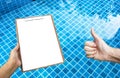 Blank paper on wooden clipboard with girl hand over crystal clear swimming pool water Royalty Free Stock Photo