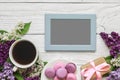 Blank photo frame with lilac flowers, coffee cup, sweet macarons and gift box on white wooden background Royalty Free Stock Photo