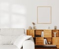 Blank picture frame mock up above wooden cupboard with decor on white wall with sunlight, gray sofa Royalty Free Stock Photo