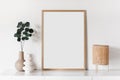 Empty vertical frame mockup in modern minimalist interior with plant in trendy vase on white wall background.