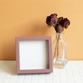 Blank picture frame and red dry rose on white table. orange wall background. copy space Royalty Free Stock Photo