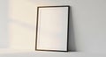 A blank picture frame with a thin black border rests against a light-colored wall. It\'s Royalty Free Stock Photo