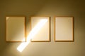Three blank wooden frames hanging on a minimalist wall with a diagonal sunbeam highlighting one canvas Royalty Free Stock Photo