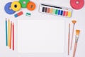 Blank piece of paper with colorful pencils, brushes and watercolors on kid`s desk