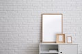 Blank poster and photo frames on cabinet near white brick wall in room. Mockup for design Royalty Free Stock Photo