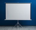 Blank projection screen near blue wall indoors Royalty Free Stock Photo