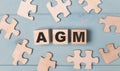 Blank puzzles and wooden cubes with the text AGM Annual General Meeting lie on a light blue background Royalty Free Stock Photo