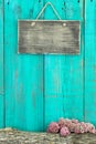 Blank rustic sign hanging on antique teal blue wood fence with log and pink flower border