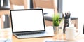 Blank screen computer laptop putting on wooden working desk and surrounded by potted plant, pencil holder and ceramic coffee. Royalty Free Stock Photo